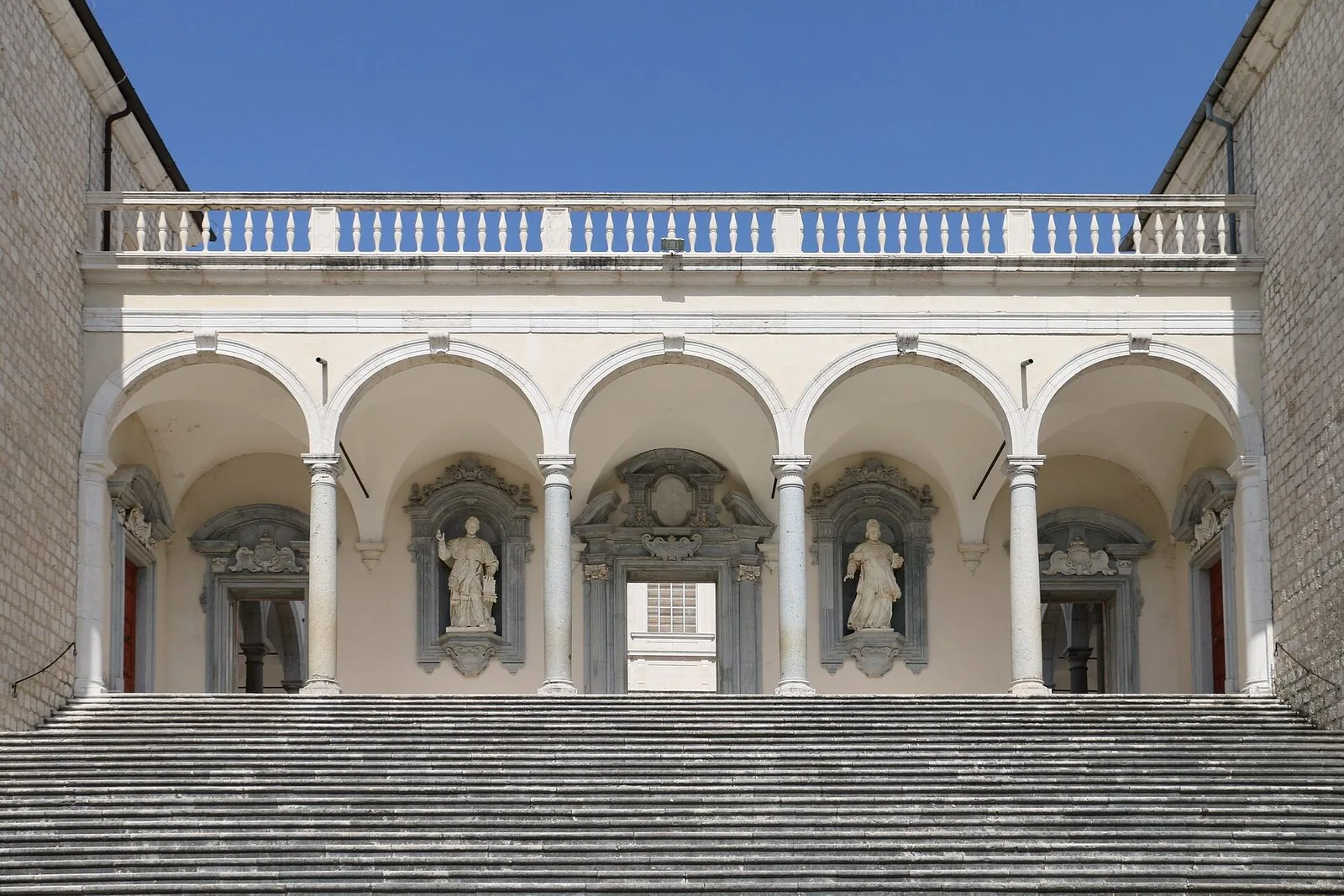 Loggiato ad archi con statue nelle nicchie in cima a un'ampia scalinata di pietra, nel chiostro del Bramante dell'Abbazia di Montecassino