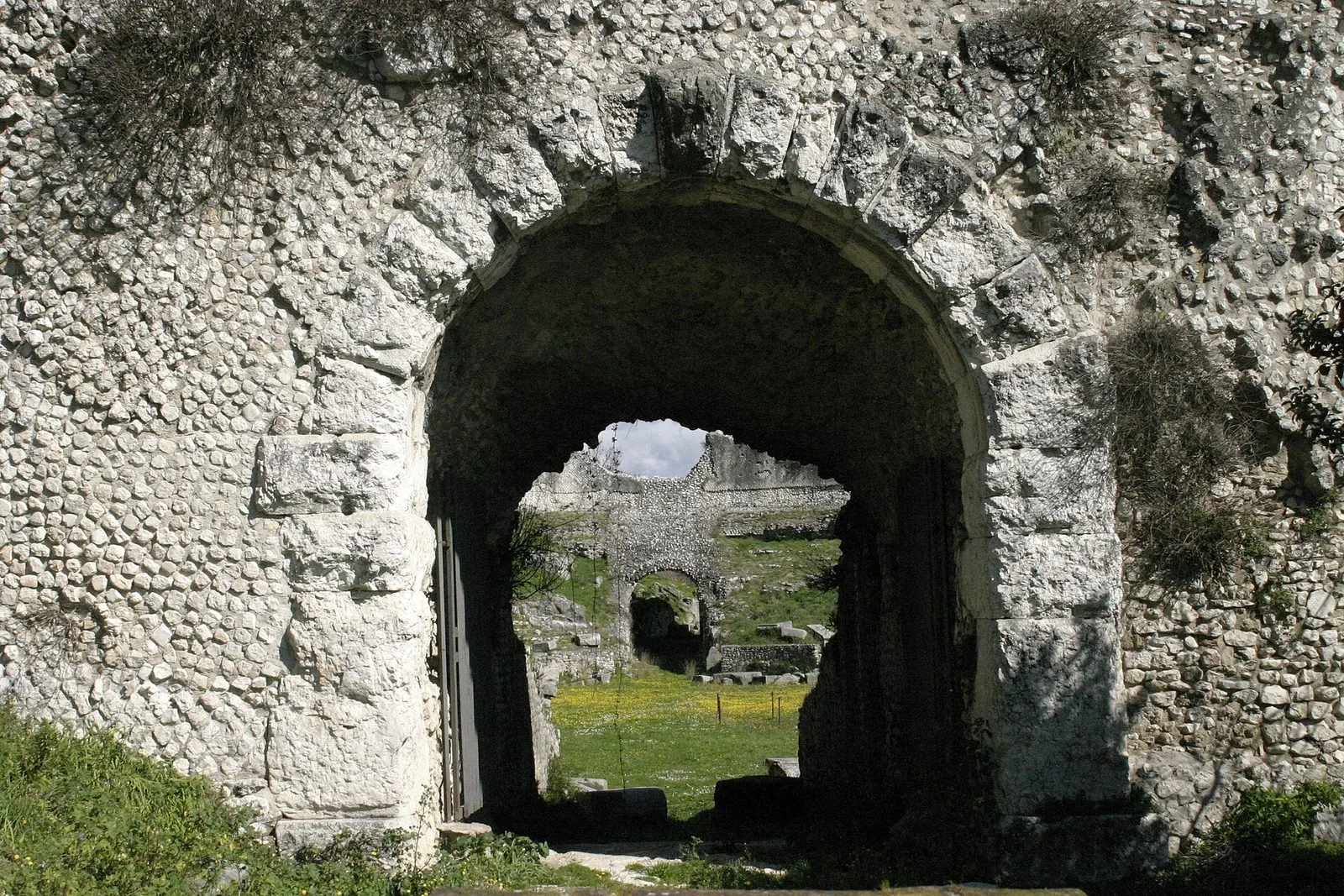 Ingresso ad arco in blocchi di pietra dell'anfiteatro romano di Casinum, con l'arena erbosa e i resti delle mura visibili attraverso l'apertura