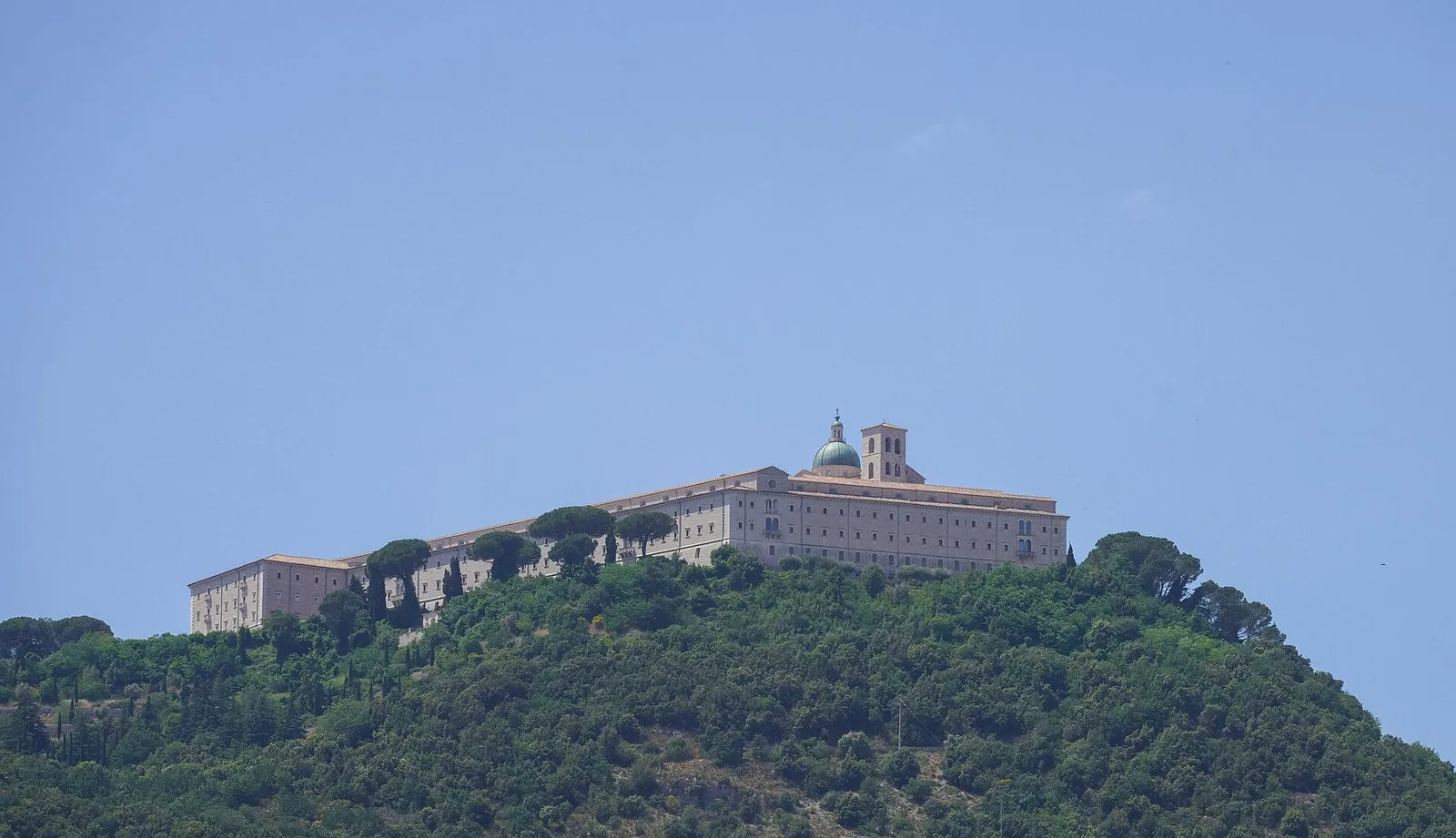L'Abbazia di Montecassino sulla sommità del monte, circondata dal bosco, sotto un cielo sereno