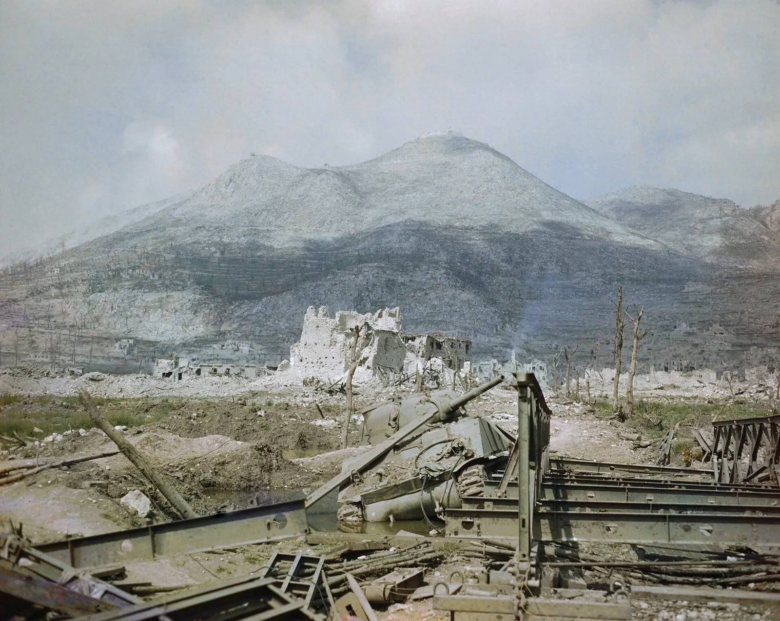 Le rovine di Cassino nel maggio 1944: un carro armato Sherman distrutto e un ponte Bailey in primo piano, le macerie della città e il monte dell'Abbazia sullo sfondo