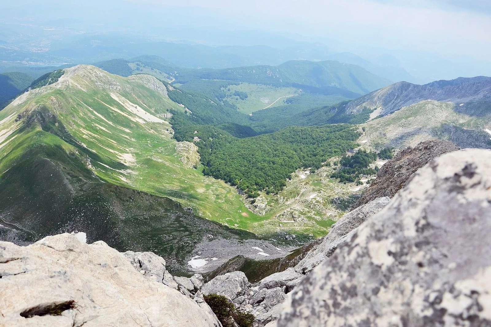 Panorama dalla vetta del Monte Meta: rocce calcaree in primo piano, creste erbose e valli ricoperte di boschi che si perdono all'orizzonte